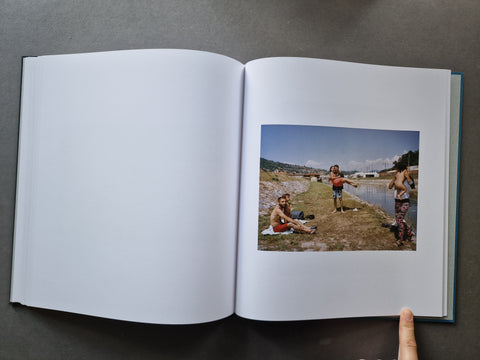 An open book, showing a blank white left page and a printed photograph on the right page of three people outdoors near water. 