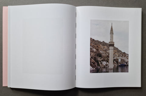 An open book showing a mostly blank white left page and a printed photograph on the right page of a coastal scene with a tall white minaret tower, rocky cliffs, and water.