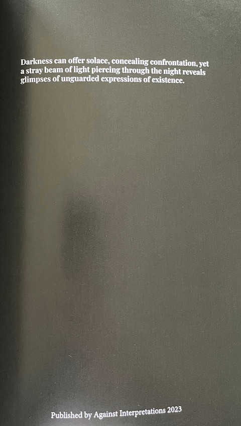 An open book or booklet showing a dark gray page with small white text, photographed against a light gray surface.