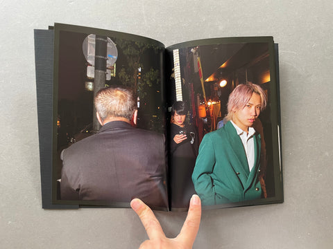 An open photo book or magazine lying on a gray surface, showing a street scene in Osaka on the pages. A hand is visible holding the bottom edge of the book.