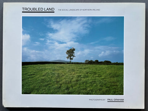 Book titled 'Troubled Land: The Social Landscape of Northern Ireland' by Paul Graham with a white cover and an image of a tree in a field.
