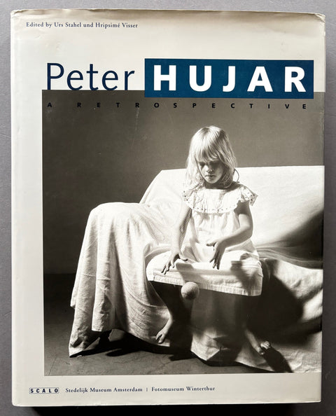 Book titled 'Peter Hujar: A Retrospective' with a white cover featuring the image of a girl sitting on a sofa bouncing a ball against the floor.