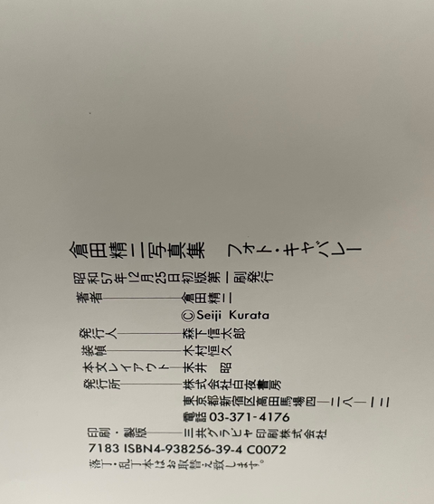 A close-up of a white printed card or booklet page with black Japanese text, resting on a dark surface with a yellow strip visible along the bottom edge.