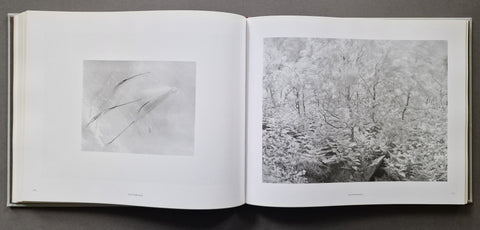 An open book showing two monochrome art prints on white pages, photographed from above on a dark gray surface.