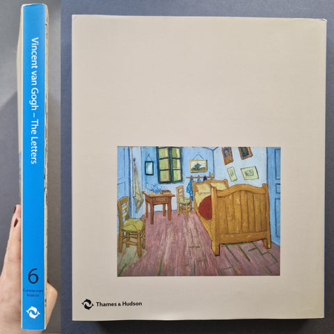 A hardcover book titled 'Vincent van Gogh - The Letters' shown standing upright, with a hand holding the blue left spine edge for scale. The front cover has a large cream background and a central reproduction of Van Gogh's bedroom painting.