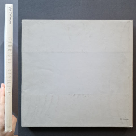 A square, light gray textured book or art print shown from the back, with its spine visible on the left against a dark background. The spine reads 'port di mare' and 'GABRIELLE BASILICO'.