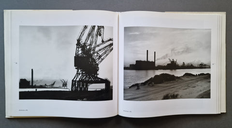 An open book showing two black-and-white photographic prints side by side, photographed from above on a dark gray surface.