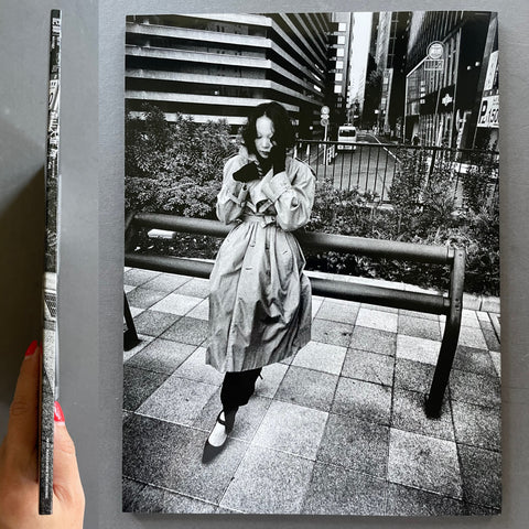 Person in a trench coat standing on a city street with a black and white photo of the same scene on a book cover.