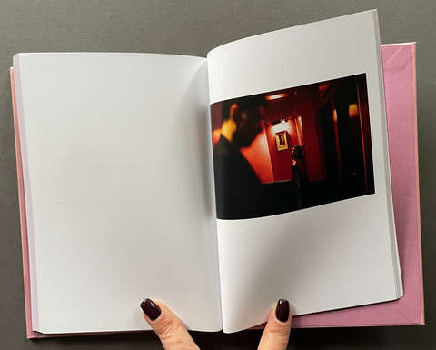 An open hardcover book with white pages, featuring a printed photograph of a dimly lit hallway on the right page. 