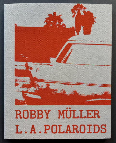 Book titled 'L.A. Polaroids' by Robby Müller with a white cover featuring the image of a car, a building and some palm trees printed in red.