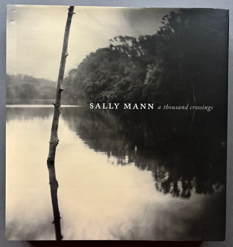 Book titled 'A Thousand Crossings' by Sally Mann with a cover featuring the image of a body of water with the surrounding fauna reflected in its surface.
