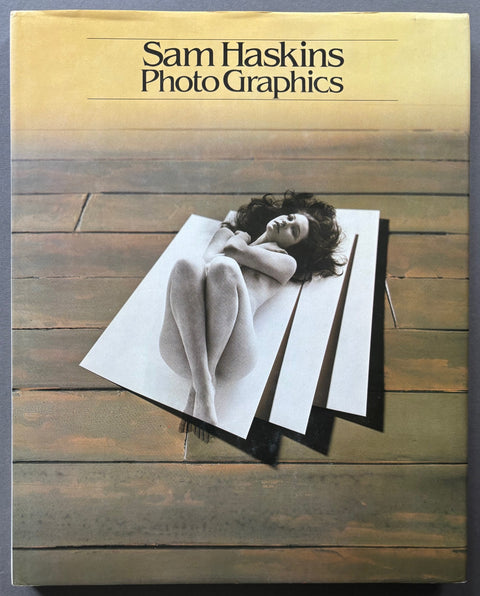 Book titled 'Photo Graphics' by Sam Haskins with a photograph of a naked woman lying modestly on a background of floorboards.