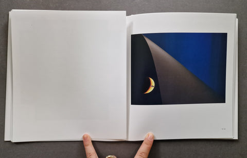 An open book showing a blank white left page and a printed spread with a dark abstract photograph of a crescent moon on the right page