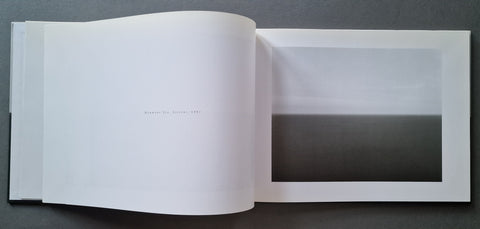 An open art book, showing a minimalist black-and-white landscape photograph printed on one page with a large white margin.