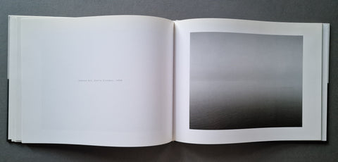 An open book showing a minimalist black-and-white landscape photograph on the right page, photographed from above on a dark gray surface.