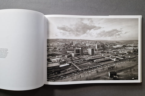 An open book showing a black-and-white cityscape photograph printed on the right page, photographed from above on a dark gray surface.