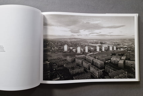 An open book showing a black-and-white architectural cityscape photograph printed on the right page, photographed from above on a dark gray surface.