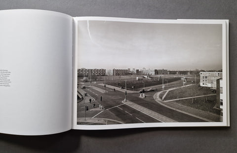 An open book spread showing a black-and-white architectural photograph of a city intersection and apartment buildings, photographed from above on a dark gray surface.