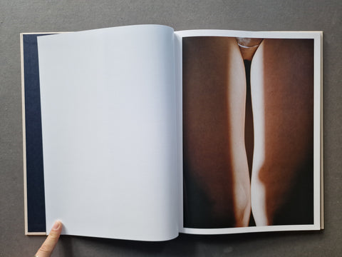 An open art book  showing a blank white page on the left and a photographic print of a close-up body image on the right. 
