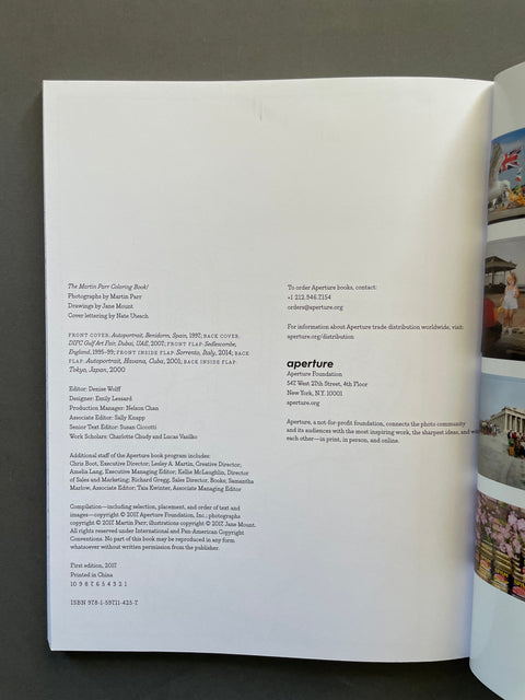 An open book spread photographed from above on a dark surface. The left page contains multiple columns of small black text, and the right page shows a narrow strip of printed artwork with a red sky and buildings.