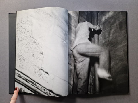 An open black-and-white art book, showing a photographic print of a person climbing or leaning against a wall on the right page.