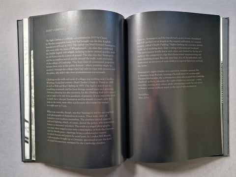 An open book spread showing two dark gray pages with small white text, photographed from above on a light gray surface.