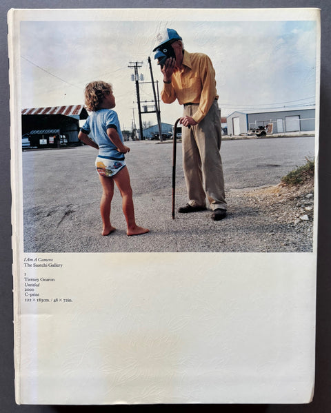 Book titled 'I Am A Camera' by The Saatchi Gallery with a white cover featuring the image of a man holding a bird mask over his face standing in front of a young boy.