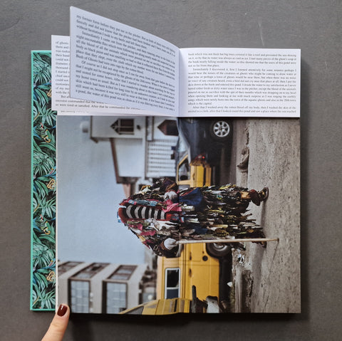 An open book, showing printed text on the left and right pages and a large photograph on the spread. The photograph depicts a person in a highly detailed, colorful futuristic suit standing beside a yellow vehicle.