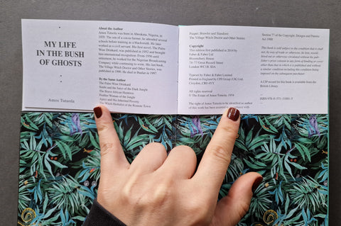 An open book or booklet laid flat on a patterned surface, with a hand holding one page. The left page reads 'MY LIFE IN THE BUSH OF GHOSTS' and the right page contains author and copyright text.