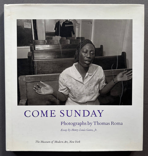 Book titled 'Come Sunday' by Thomas Roma with a white cover featuring the image of a woman sitting in a church with her eyes closed and her arms outstretched.