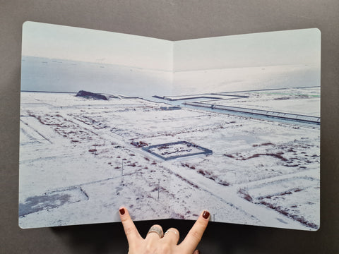 A book showing a photo of a snowy landscape with farm fields and a long structure.