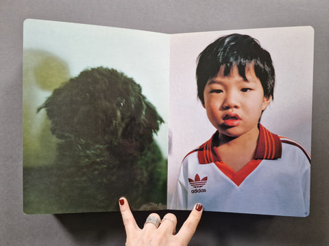 An open photo book, showing a black fluffy dog on the left page and a young boy in a white Adidas jersey on the right page. 