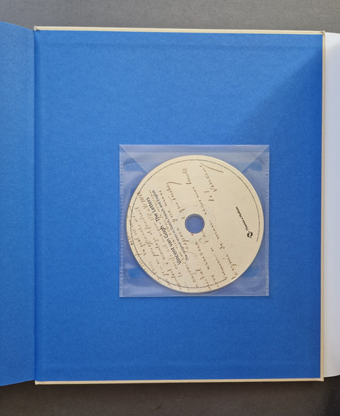 An open book or album with a bright blue cover, featuring a clear plastic sleeve holding a cream-colored printed disc in the center.