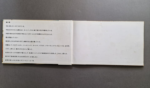 An open book spread laid flat on a dark gray surface, showing two white pages with small black Japanese text.