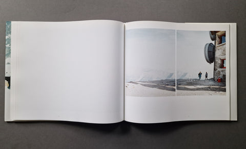 An open hardcover book, showing a mostly blank left page and a two-photo spread on the right page with a snowy landscape and a building scene.