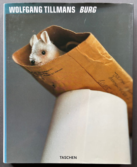 Book titled 'Burg' by Wolfgang Tillmans with a cover featuring a photograph of a toy animal inside an envelope balanced on an upturned paper cup.