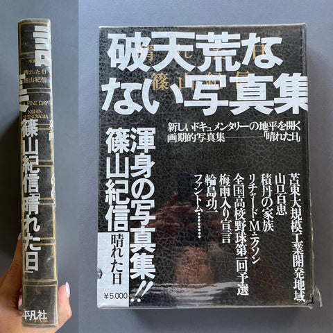 A Japanese photography book shown upright with its front cover and spine visible. A hand is holding the left edge of the book.
