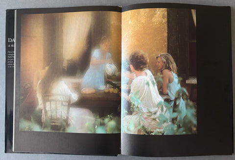An open book or magazine spread showing two printed photographs side by side. The left page has a dark border and a softly lit, painterly scene with a seated figure in a blue dress.