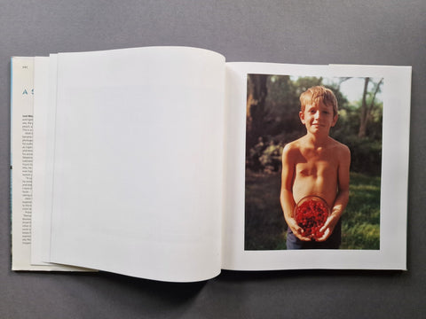 An open book, showing a large blank white page on the left and a printed photograph on the right of a shirtless boy holding a bowl of berries.