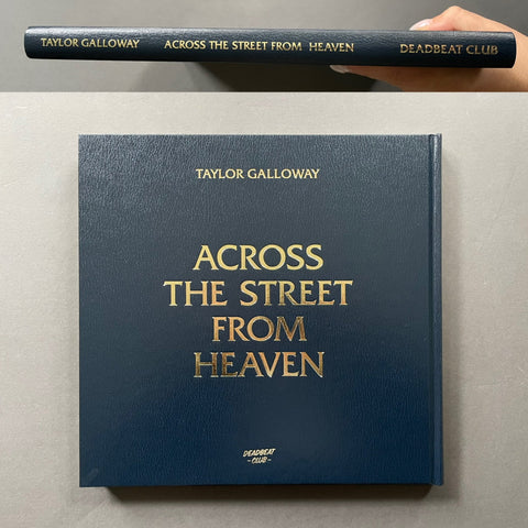 A hardcover music book titled 'Across the Street from Heaven' by Taylor Galloway, shown from the front with gold foil lettering on a dark navy cover, with a hand holding the spine at the top of the frame.