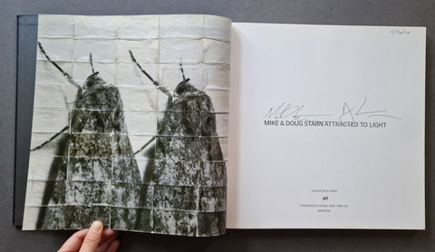 An open book  showing a black-and-white photograph of two moths on the left page and a signed title page on the right.