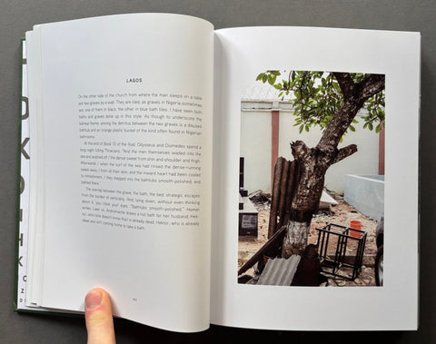 An open book showing a two-page spread with printed text on the left page and a color photograph on the right page. A person's thumb is visible holding the bottom left edge of the book against a dark gray background.