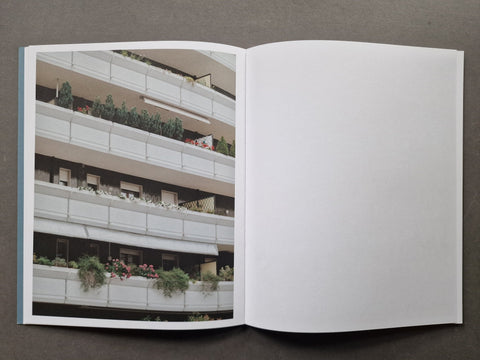 An open book, showing a printed architectural photograph of apartment balconies with plants on the left page and a blank white page on the right.