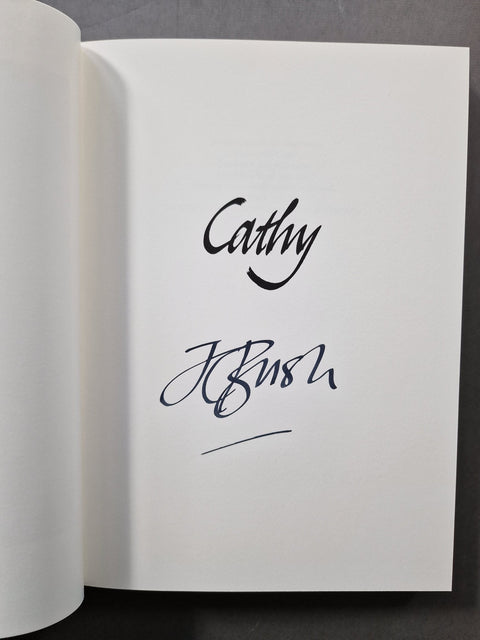 An open book k showing a white page with black cursive signatures reading 'Cathy' and 'JC Bush' on a dark gray background.