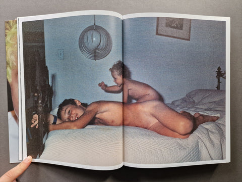 An open book showing a photographic print of two children on a bed in a dimly lit room. 