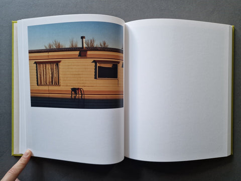 An open hardcover book - The left page shows a color photograph of a beige house exterior under a blue sky, while the right page is blank white.