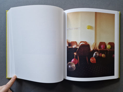 An open book - The right page contains a printed interior photograph showing chairs and colorful hanging balloons.
