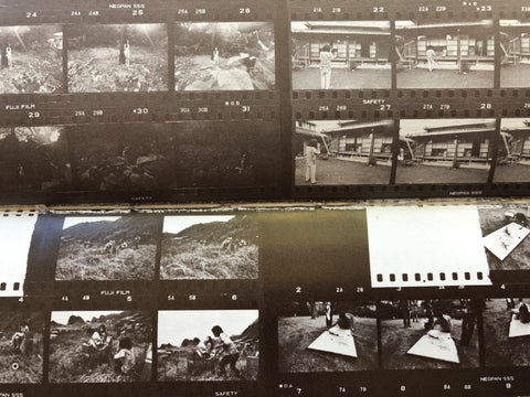 A close-up of vintage black-and-white film negatives laid out in overlapping rows, showing multiple small photographic frames with scenes of people and outdoor landscapes.