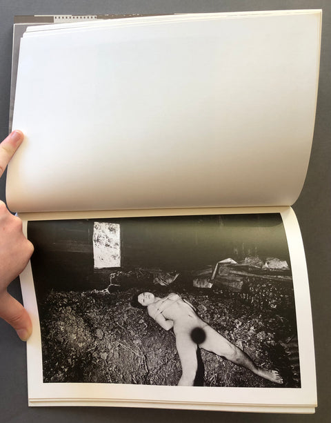 An open book or photo album showing a black-and-white photographic print on the lower page. A hand is holding the left page open.