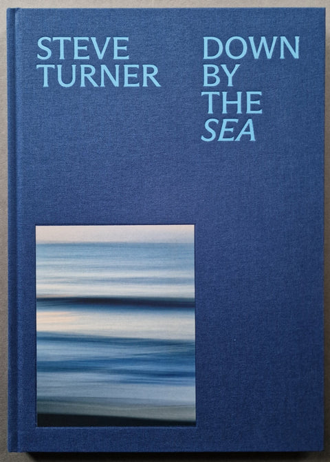 Steve Turner's book 'Down By The Sea' with a textured blue cover, featuring light blue text and a rectangular abstract photograph of water at the bottom left.